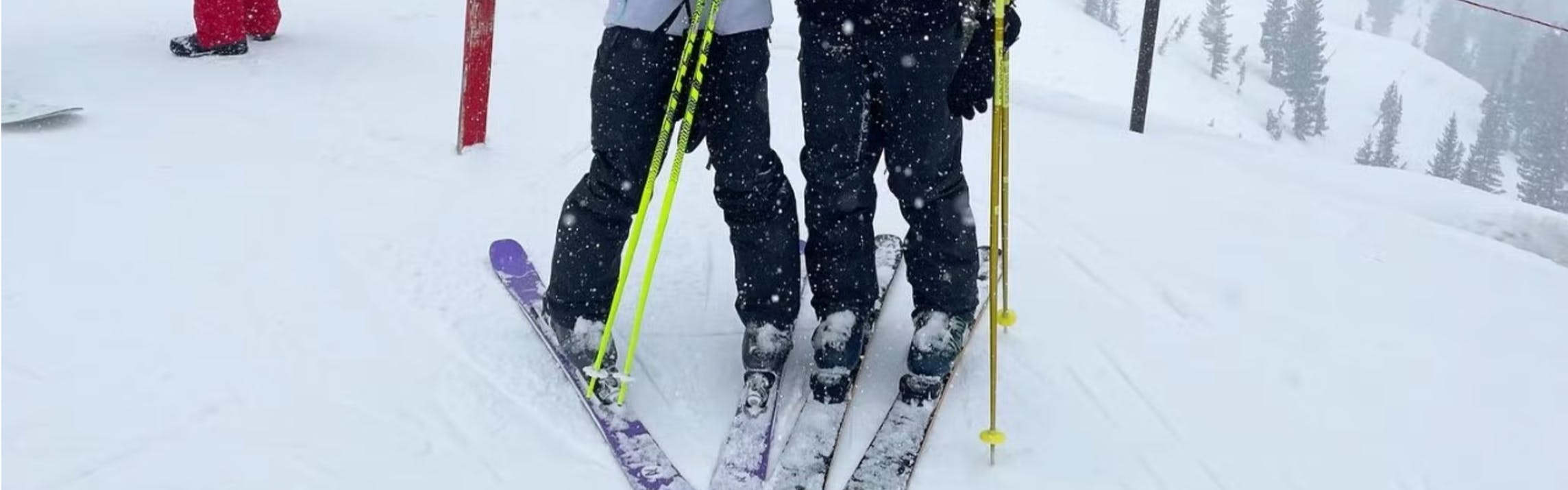 Two skiers stand on their skis. They are at a ski resort.