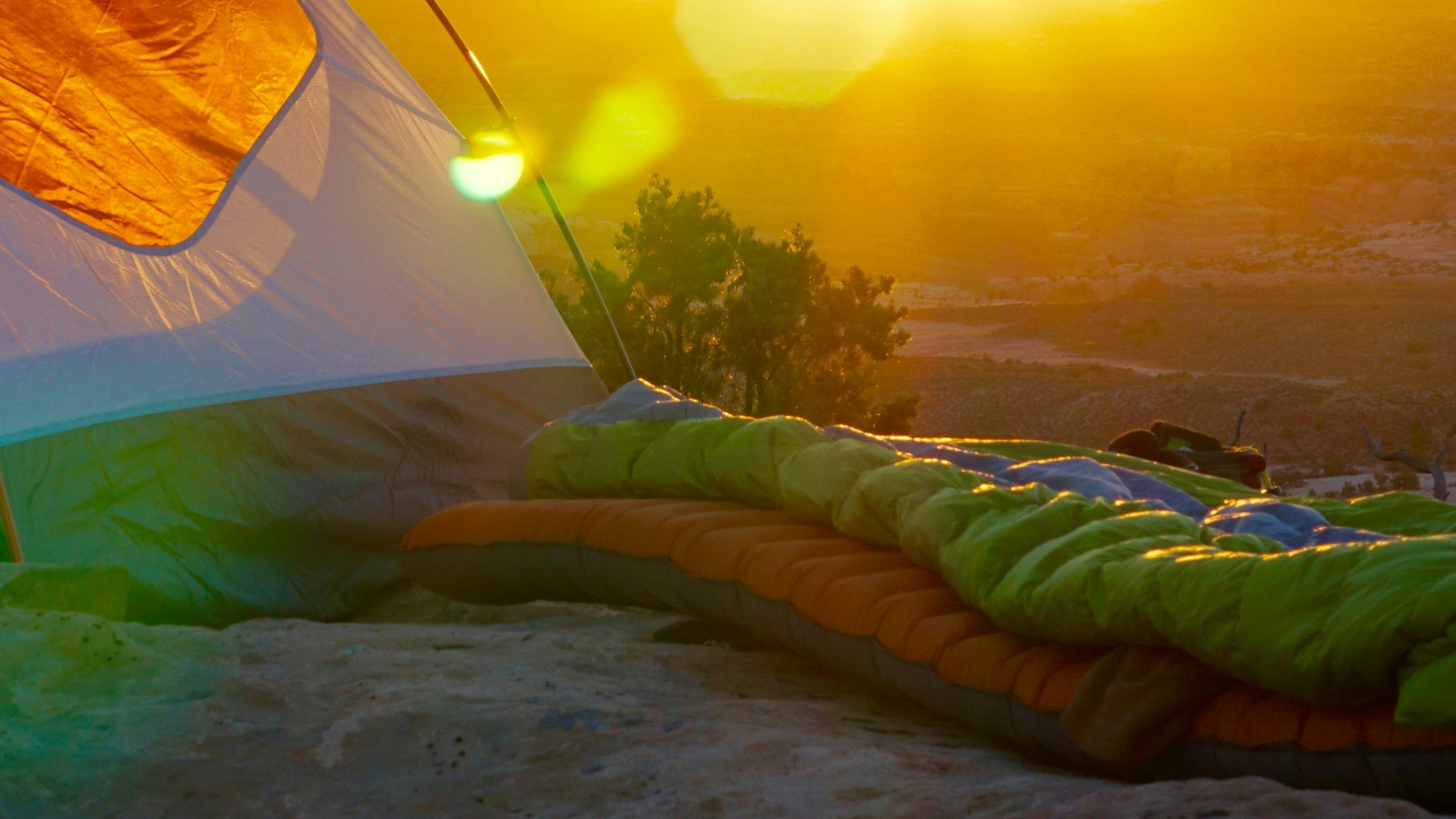 A tent with a sleeping pad and bag in front of it. There is a sunset in the background. 