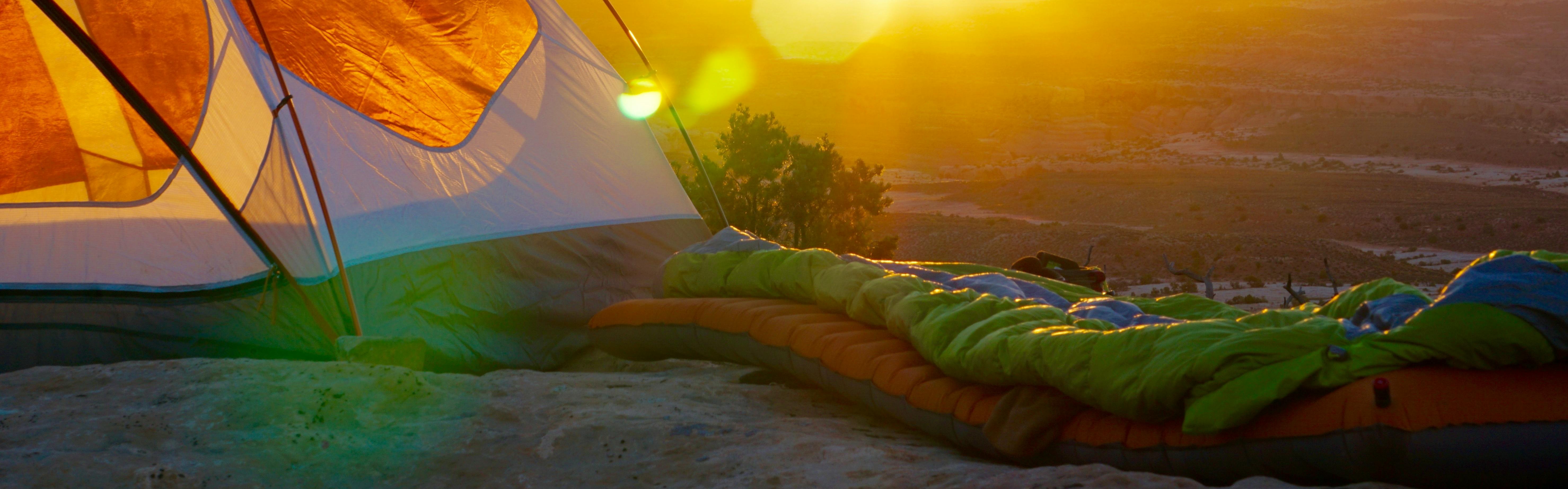 A tent with a sleeping pad and bag in front of it. There is a sunset in the background. 