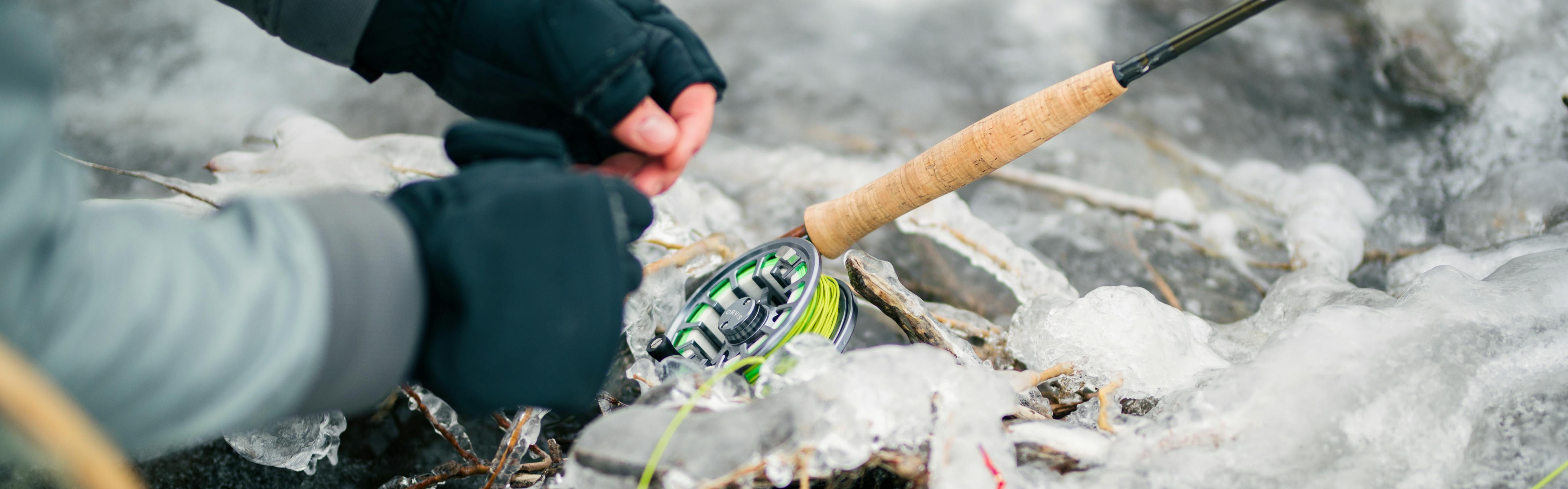 Someone handles line attached to an Orvis fly fishing reel while wearing mittens. The reel and rod are resting on ice.