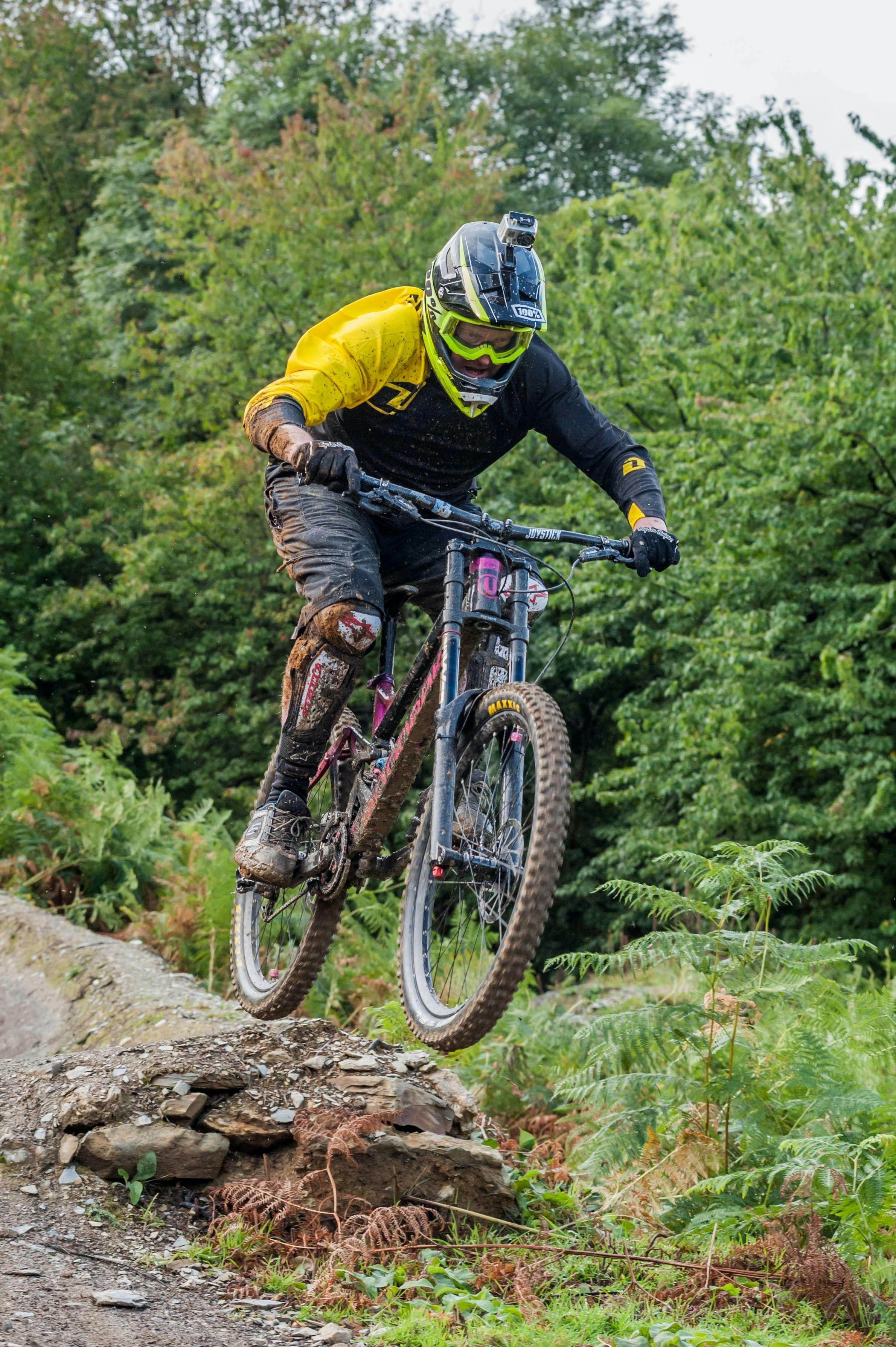 A man in a full-face helmet mountain bikes down a muddy trail