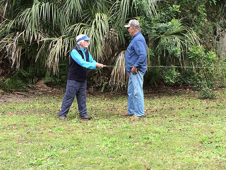 Two men stand on some grass with a fishing rod.