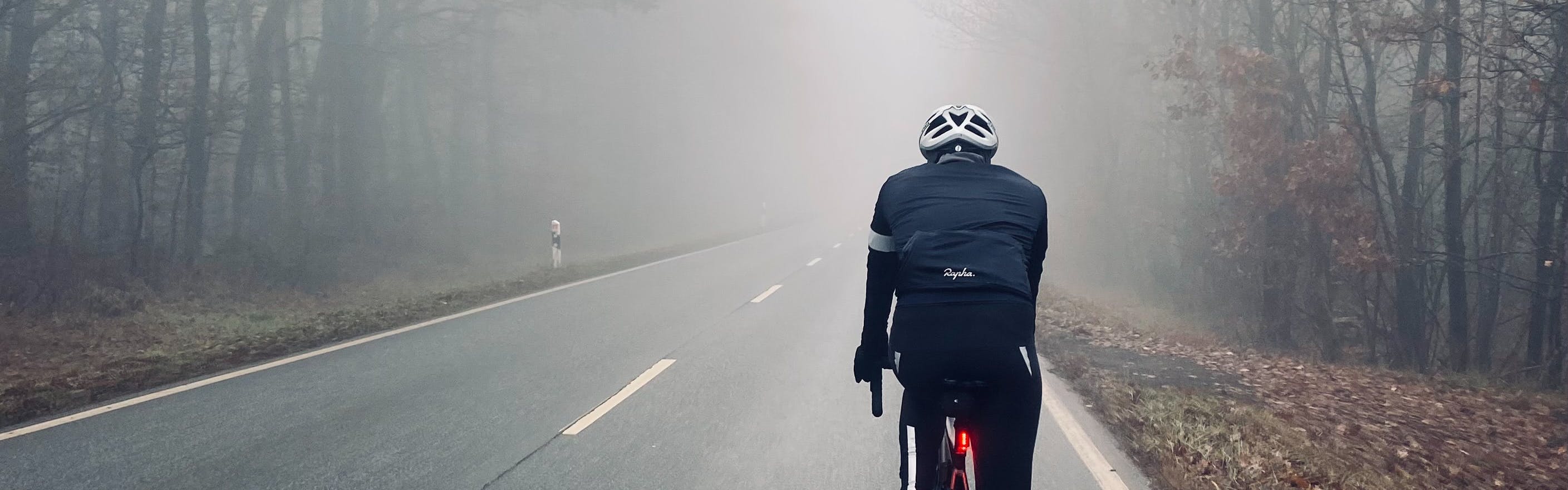 A man rides a road bike into the fog. 
