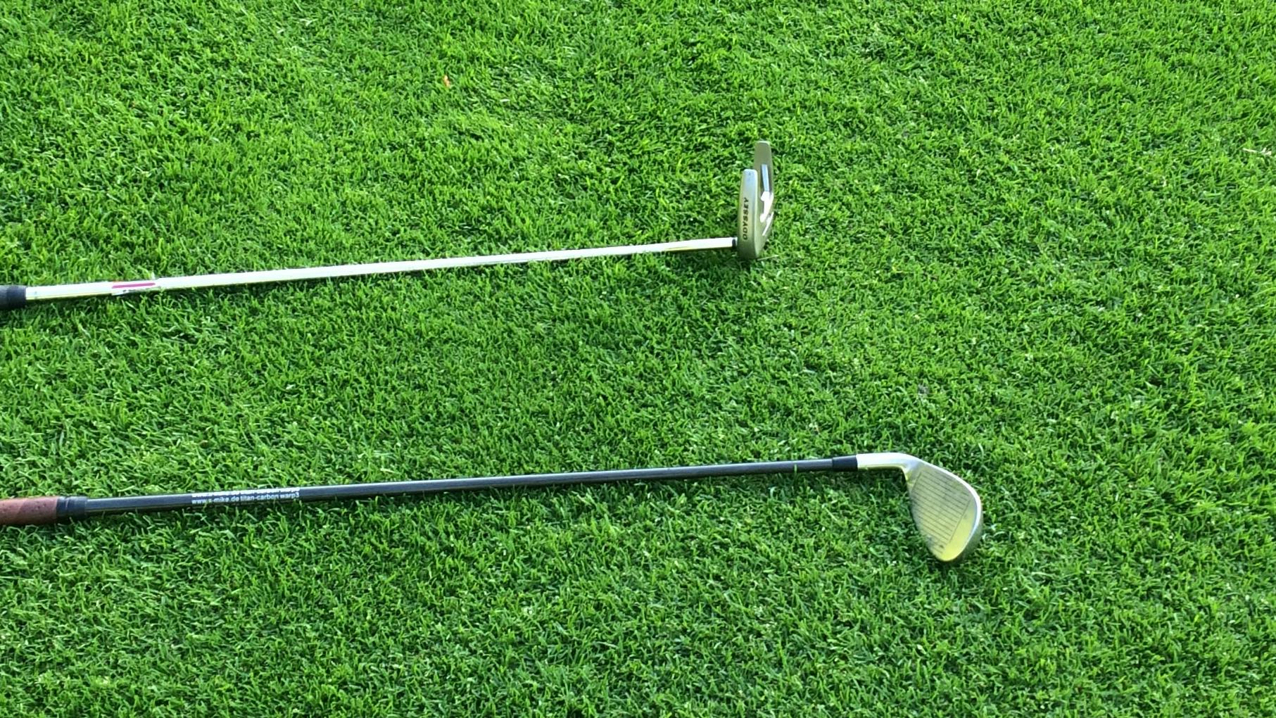 Two golf clubs lay next to each other.