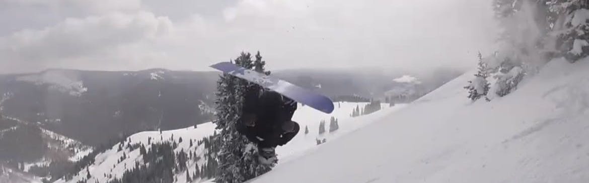 A snowboarder does a flip with her snowboard on. 