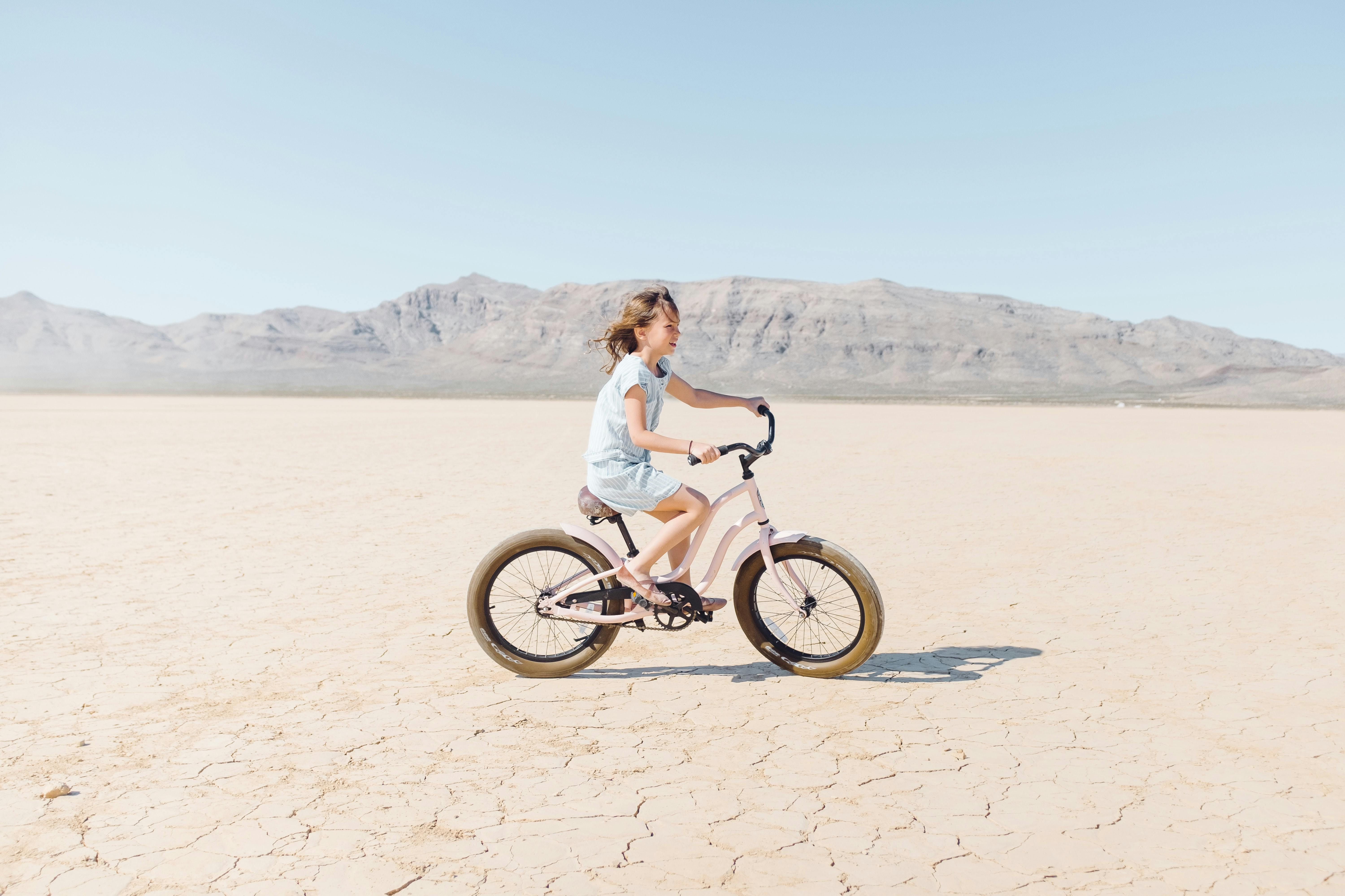 A young girl riding her bike across cracked desert earth.
