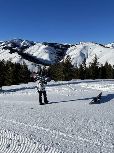 A snowboarder holding the Arbor Shiloh Camber Snowboard while standing on a ski run.  