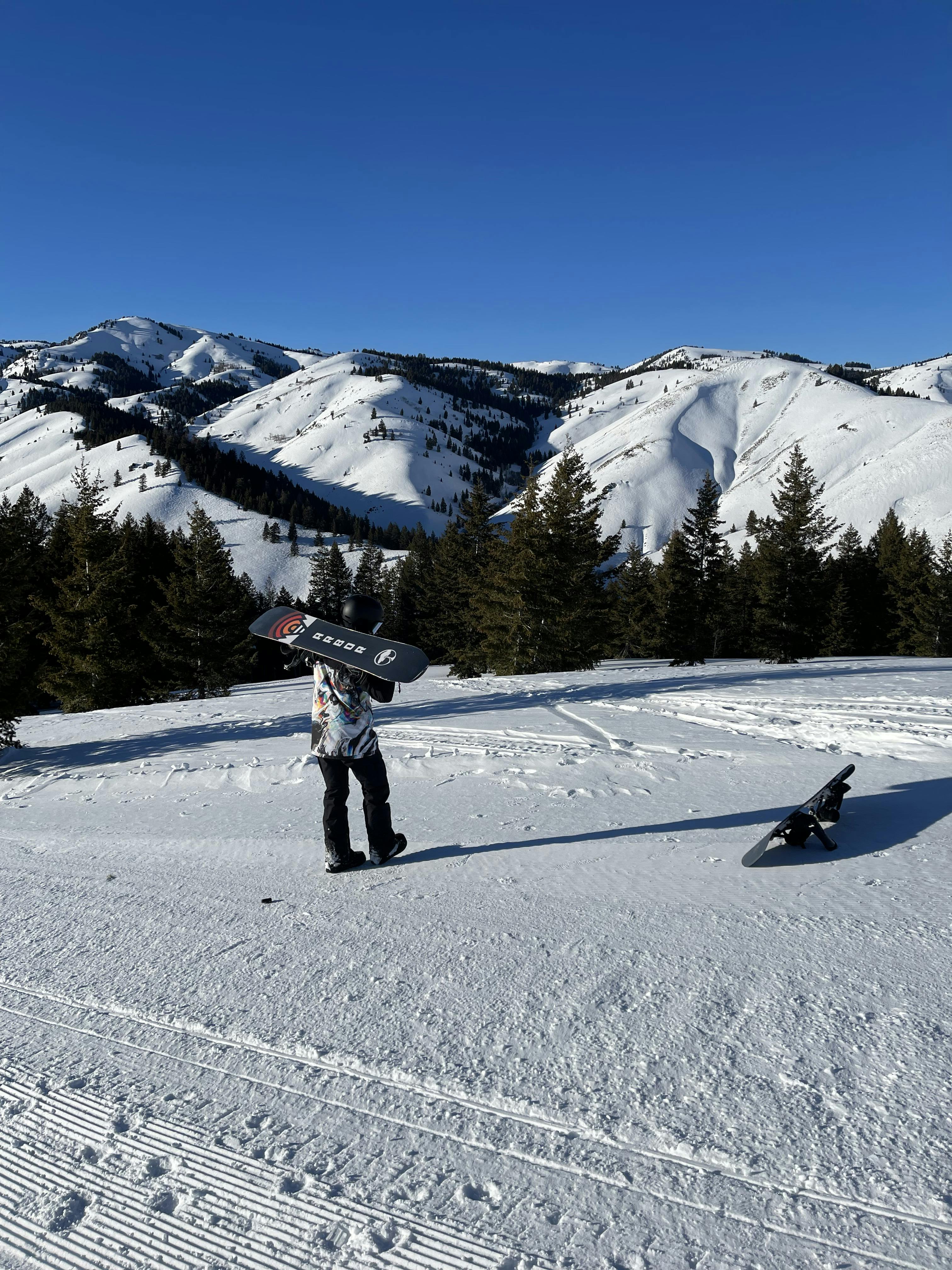 A snowboarder holding the Arbor Shiloh Camber Snowboard while standing on a ski run.  