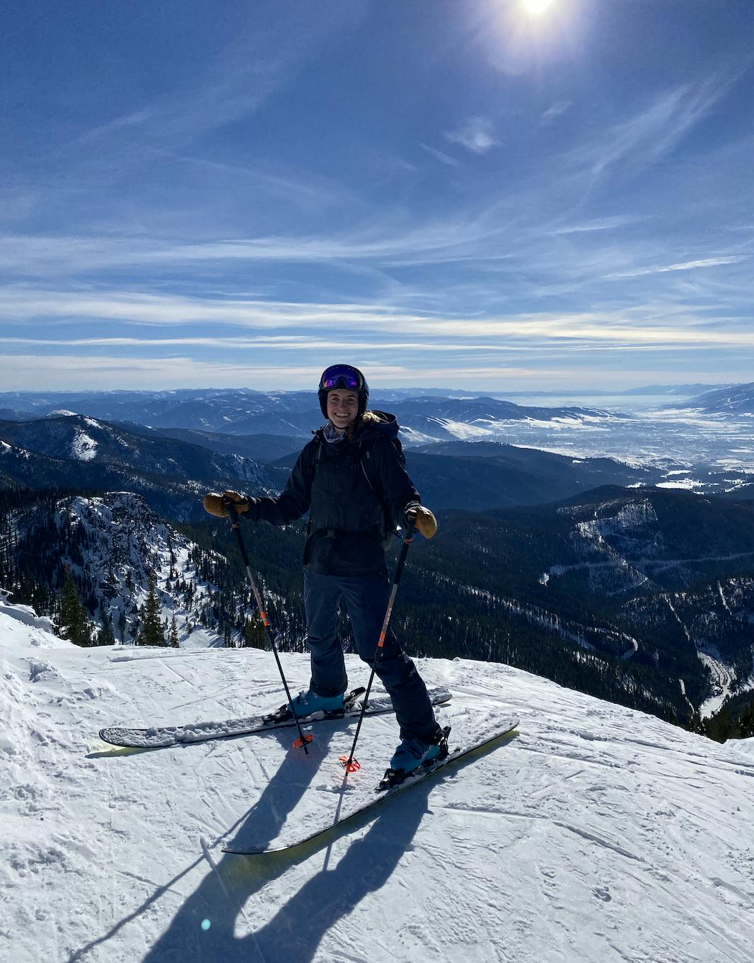 A skier standing at the top of a ski run. There are mountains in the background. 