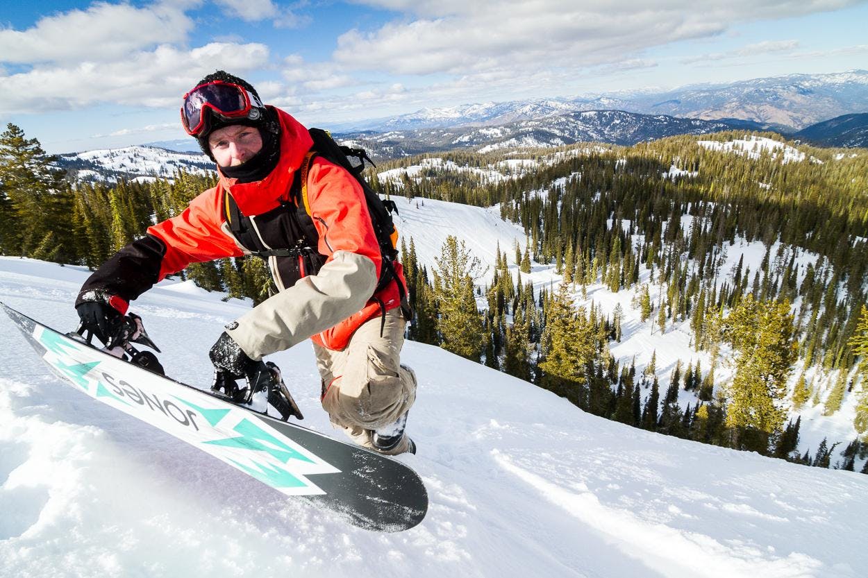 A snowboarder hiking up a mountain with his snowboard. 