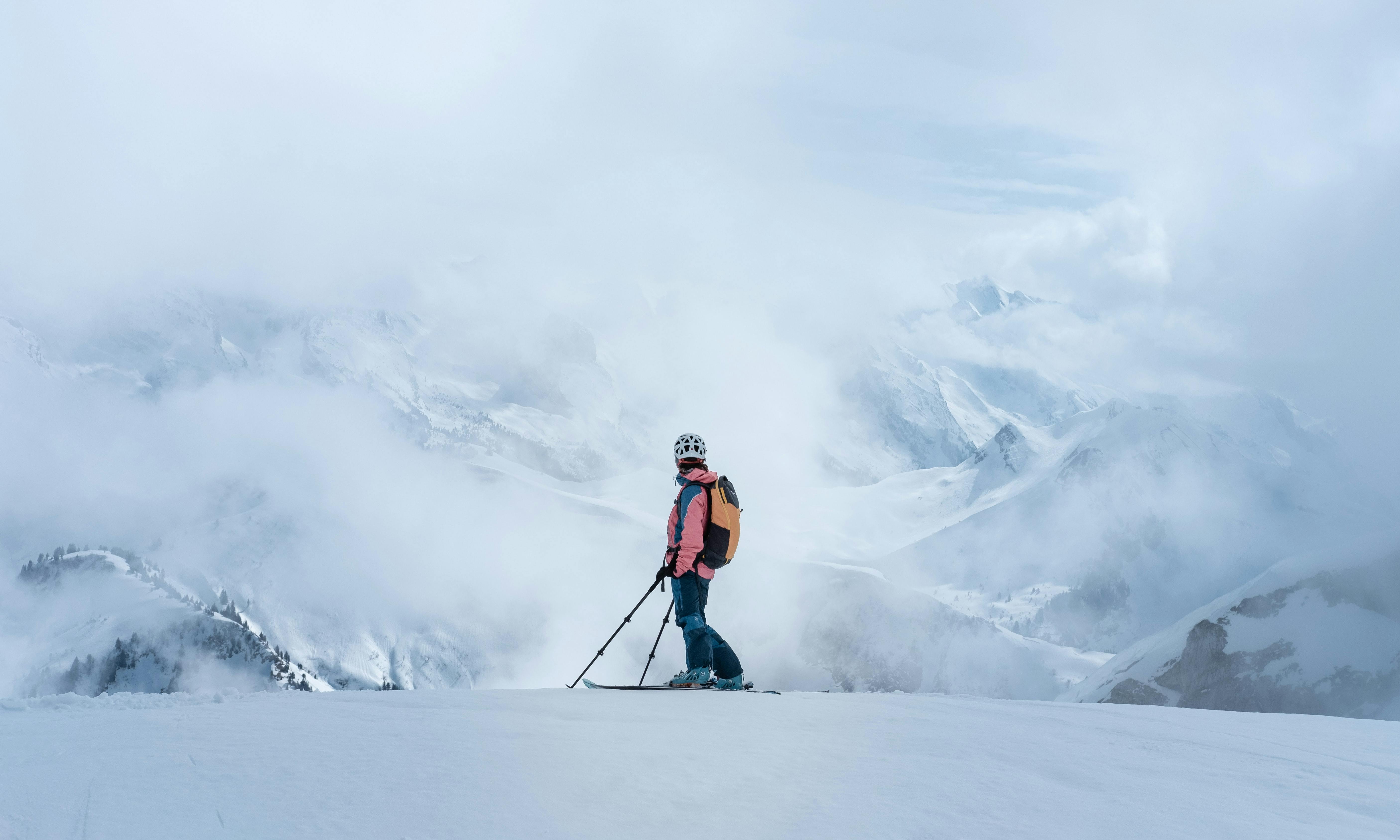 A skier stands at the top of the run. The mountains in the background are cloudy and covered in snow.