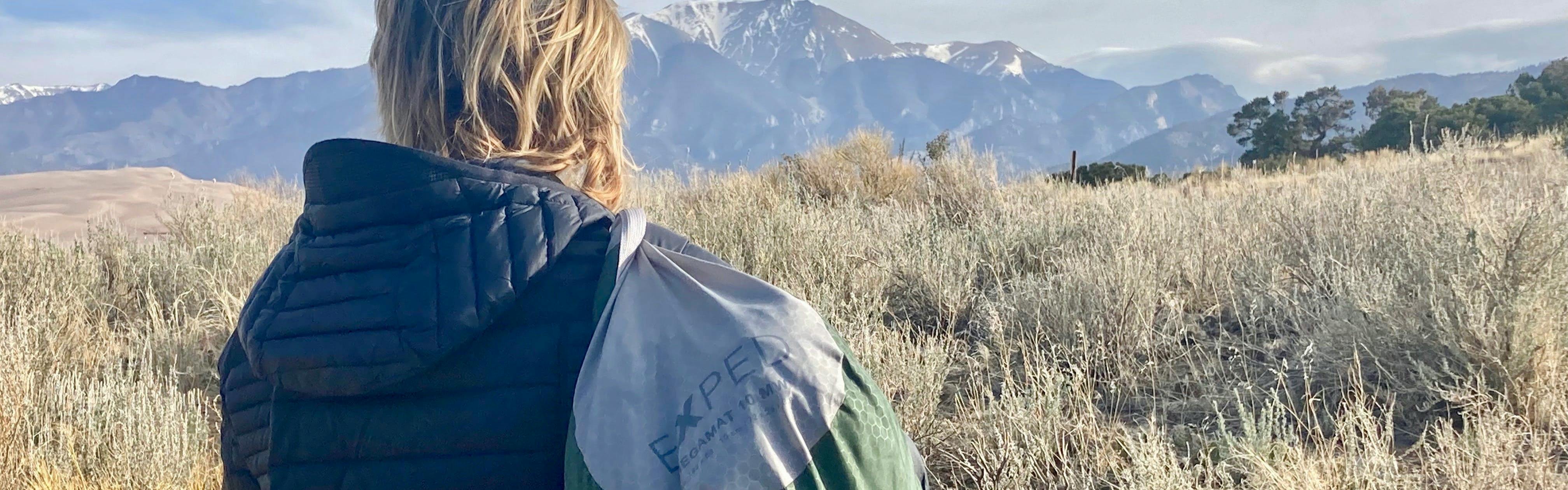 A person holds the Exped sleeping mad in its stuff sack. There are mountains in the background.