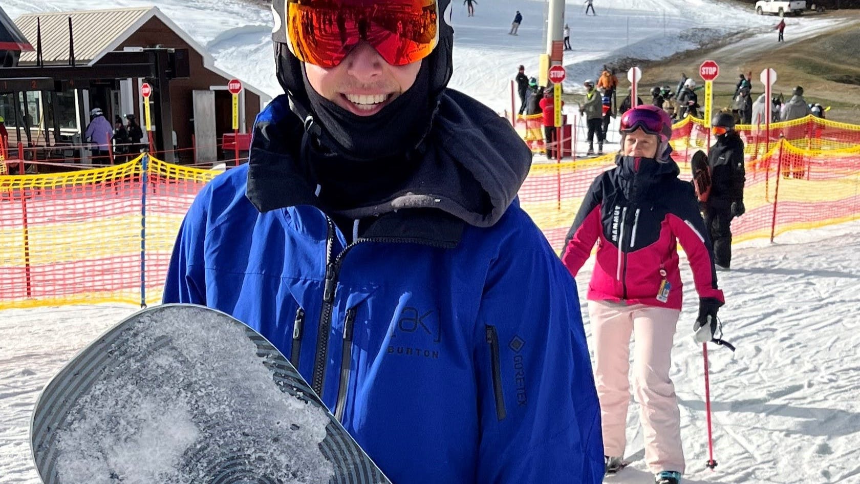 A snowboarder smiling at a ski resort while wearing the  Burton Men's [ak] Swash GORE‑TEX 2L Jacket.
