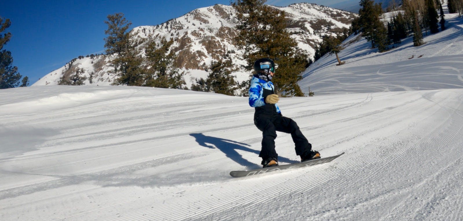 Snowboard Expert Arielle Busch riding the 2023 GNU Ladies Choice snowboard on a groomed run