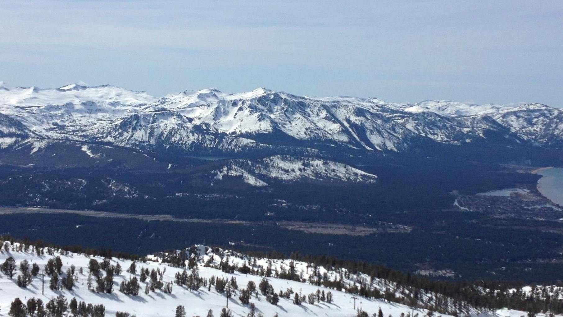 View of Lake Tahoe with snowy ski areas and mountain peaks surrounding it. 