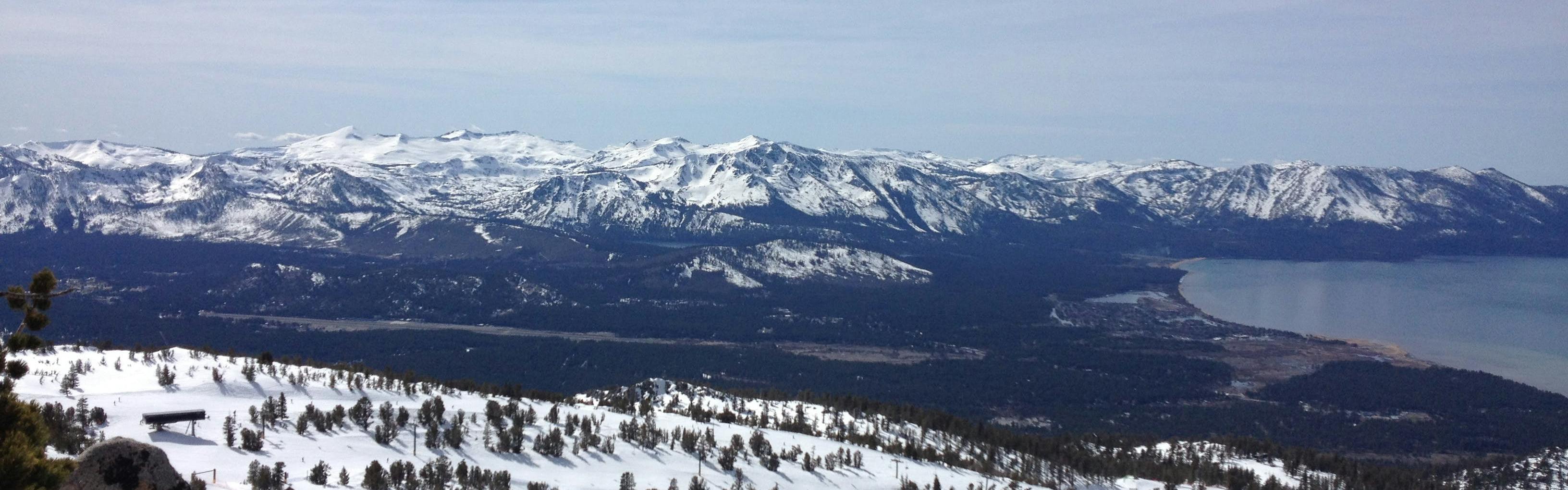 View of Lake Tahoe with snowy ski areas and mountain peaks surrounding it. 