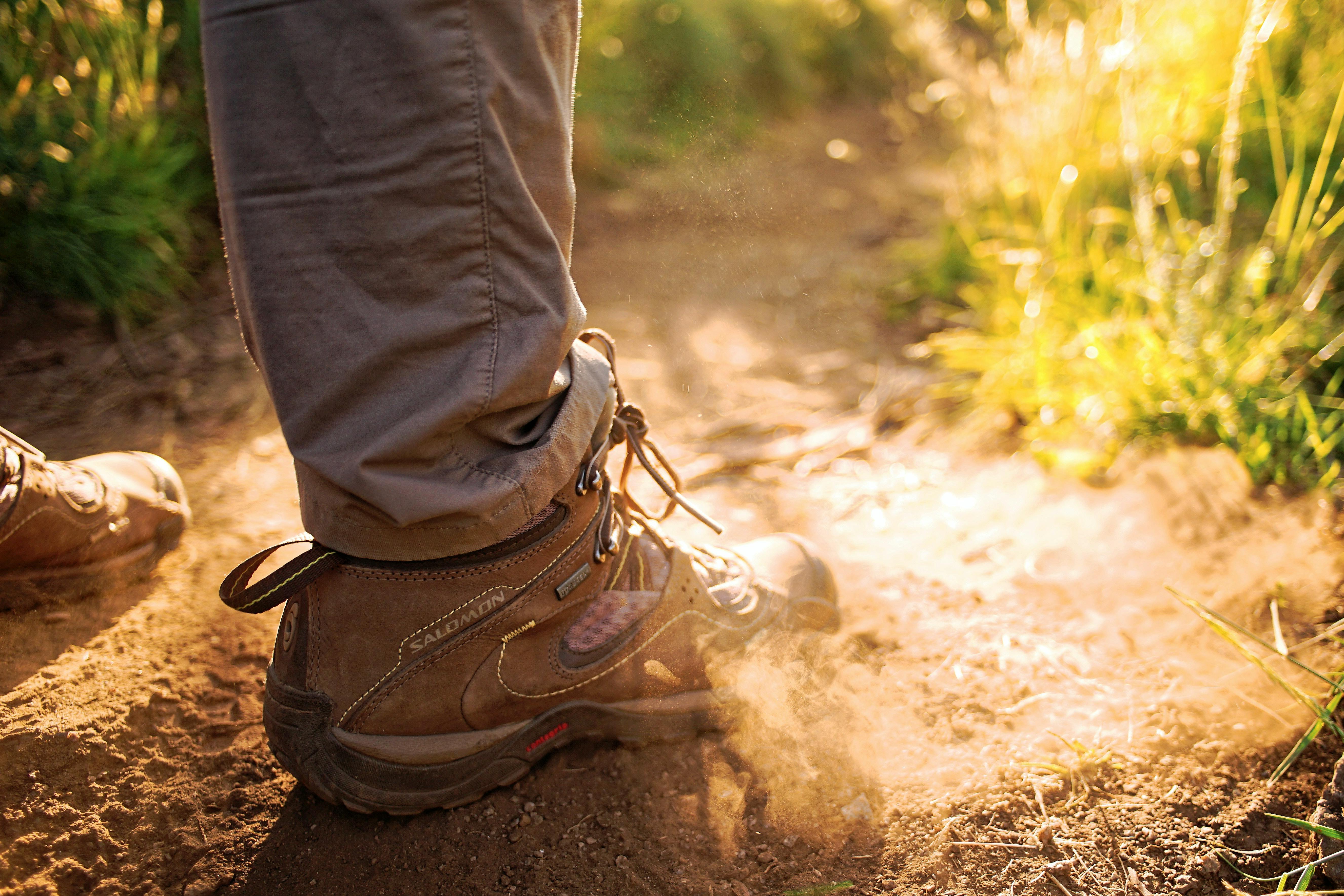 Someone stands on a trail in low Merrell hiking boots. A cloud of dust rises where their foot is. 