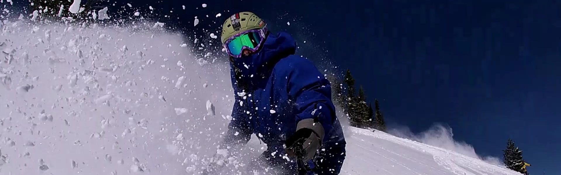 A snowboarder turning down a mountain as snow sprays him. 