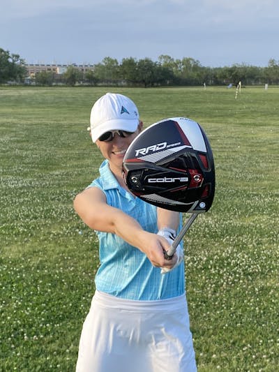 Woman on a golf course holds out the Cobra King Radspeed Driver.