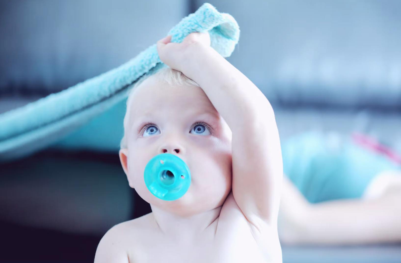 A baby with a pacifier in their mouth grabs a blanket. 