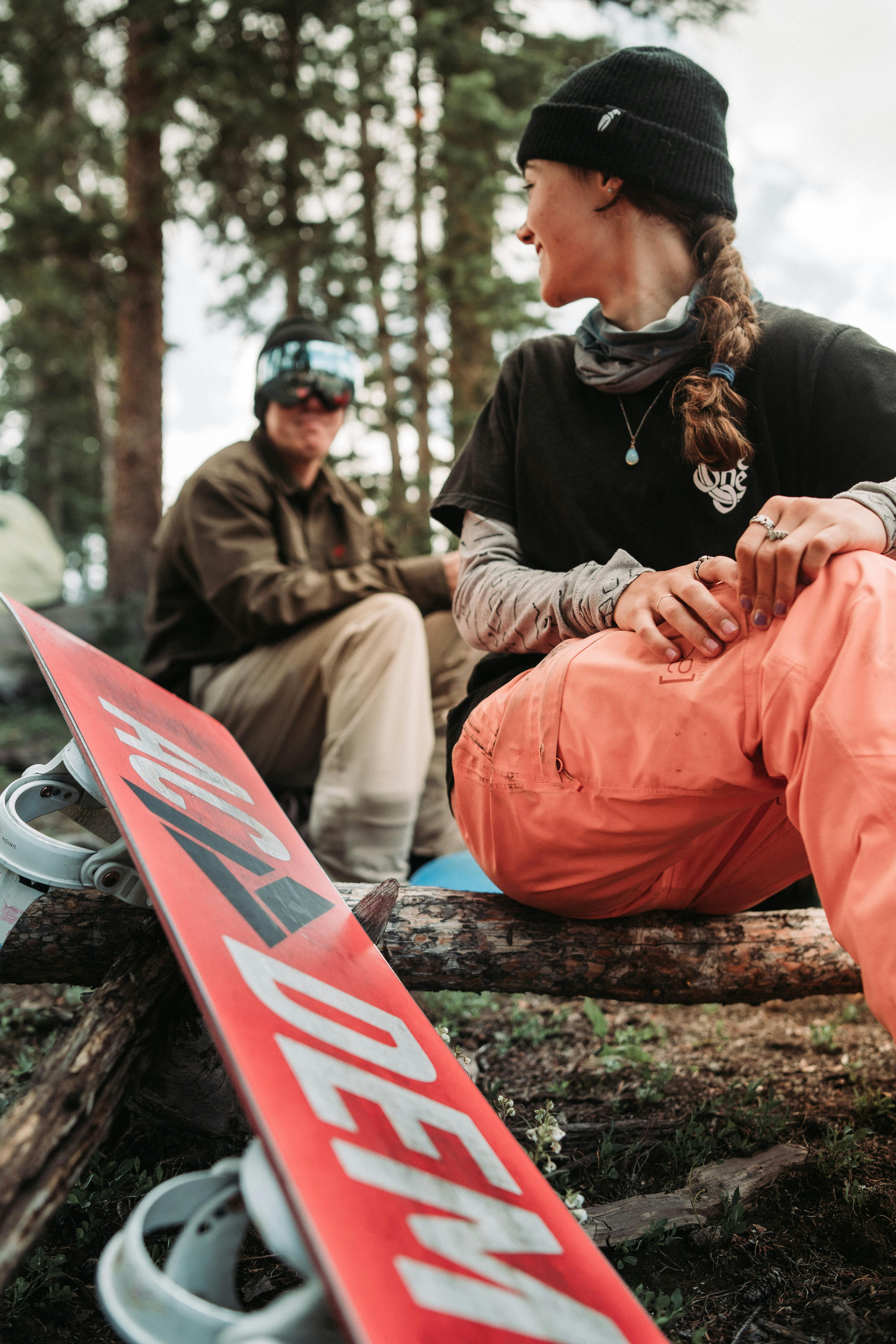 Two snowboarders sit on a log and talk.