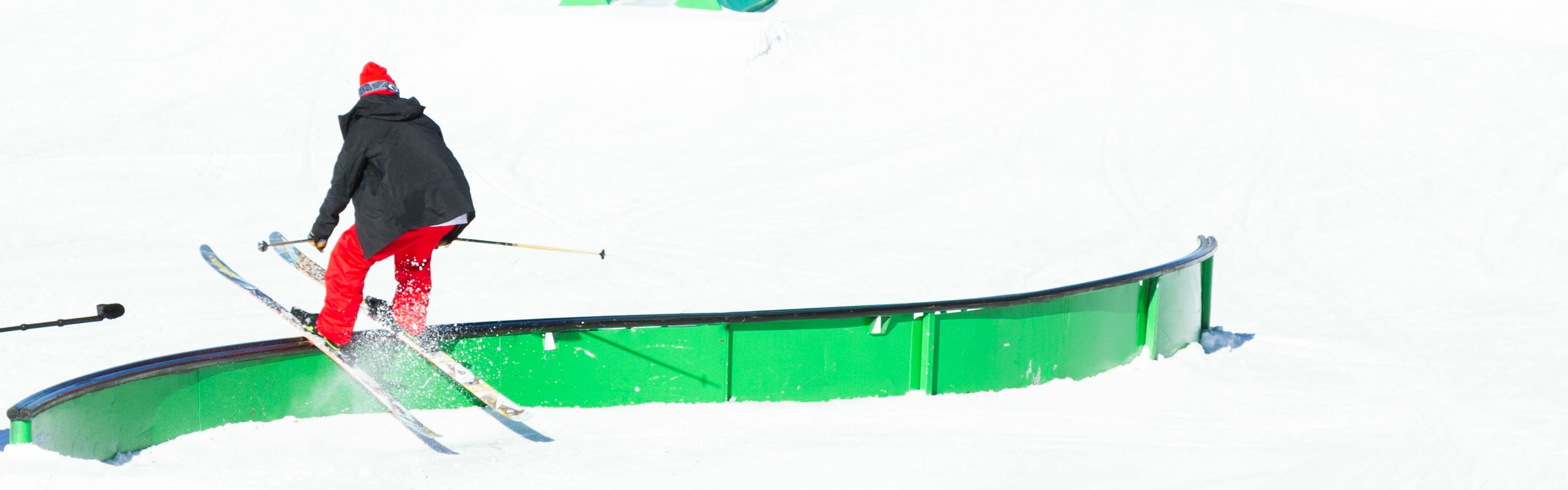 A skier in red pants slides down a green rail on his skis. 
