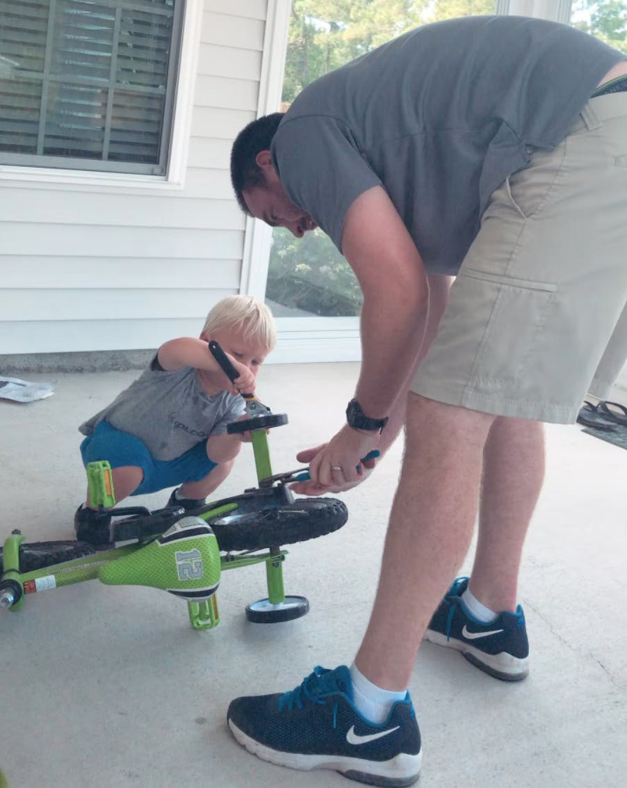 Having dad around to help you fix things is great! A child and a dad fix a bike together.