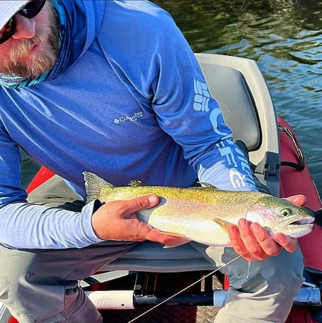 A man holding a rainbow trout in a boat. 