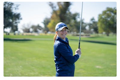 A woman holding a golf club and smiling.