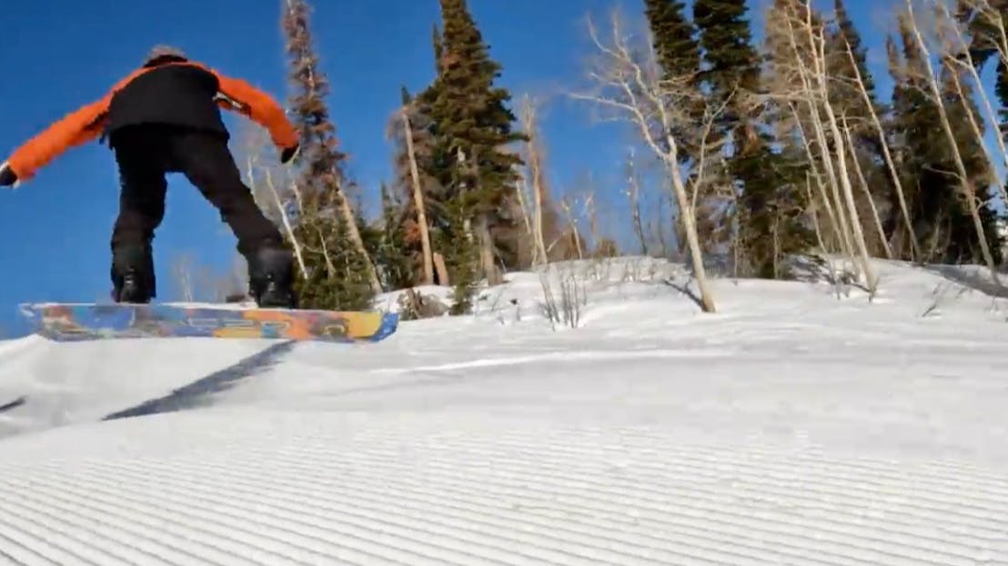 Snowboard Expert Victor Von Claus airborne with the 2023 GNU Money snowboard on a corduroy snow run