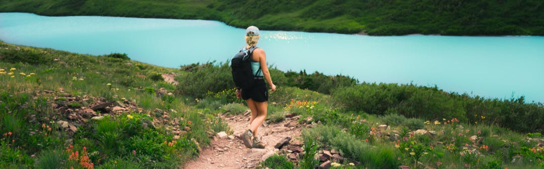A woman walking towards a lake with a backpack.