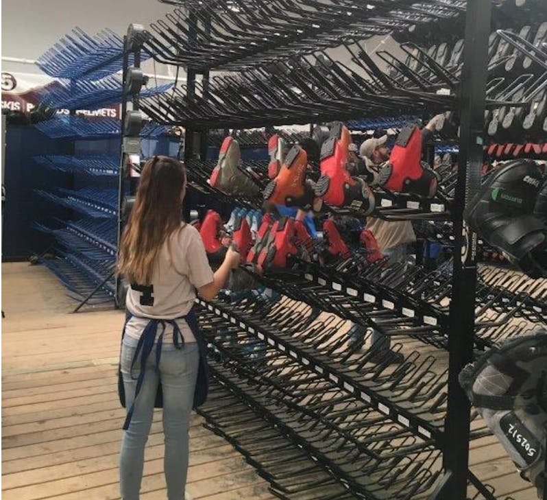 A woman putting rental boots on a rack. 