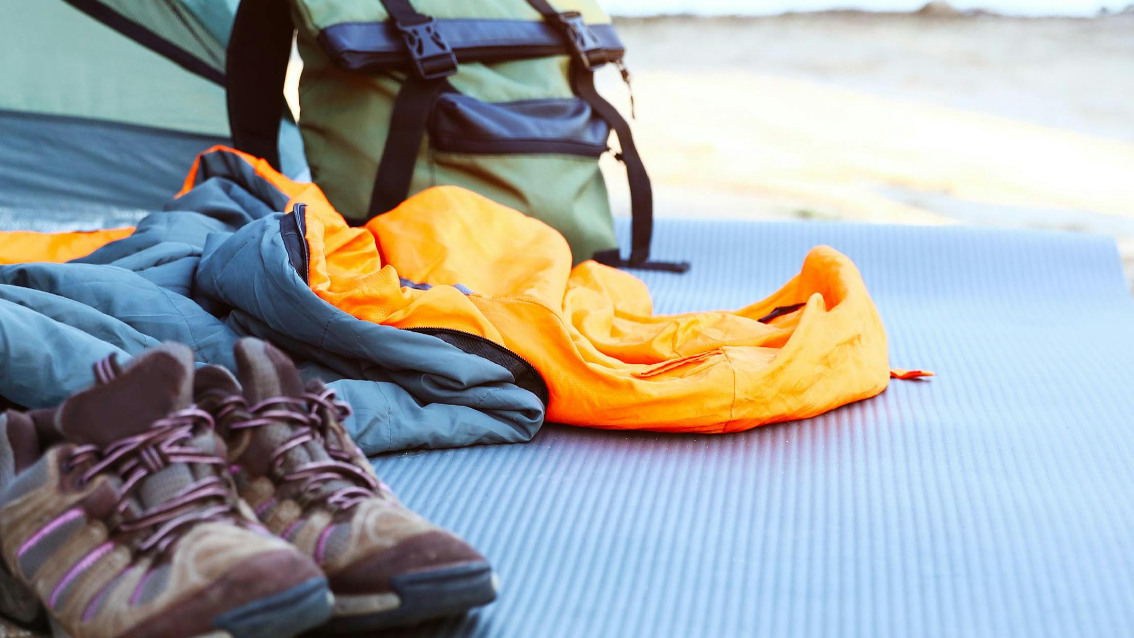 A sleeping bag spills out of a tent and onto a pad. Hiking boots and a backpack also rest on the pad. 