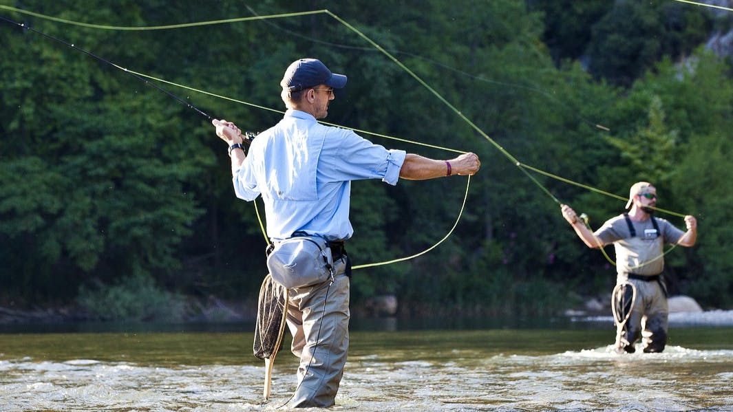 Two men cast their fly rods while wading in a river. 
