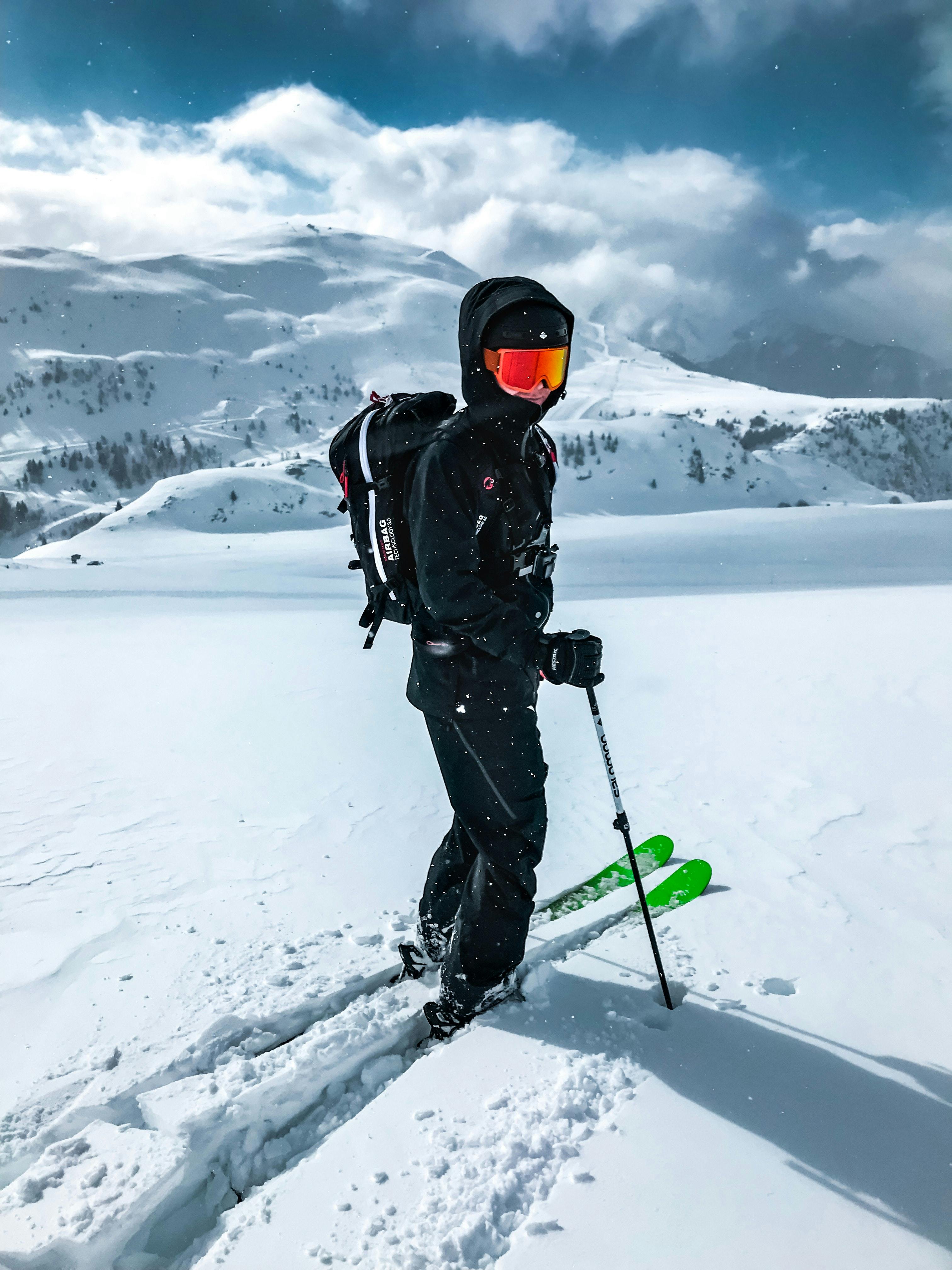 A skier in all black turns to look at the camera over their shoulder