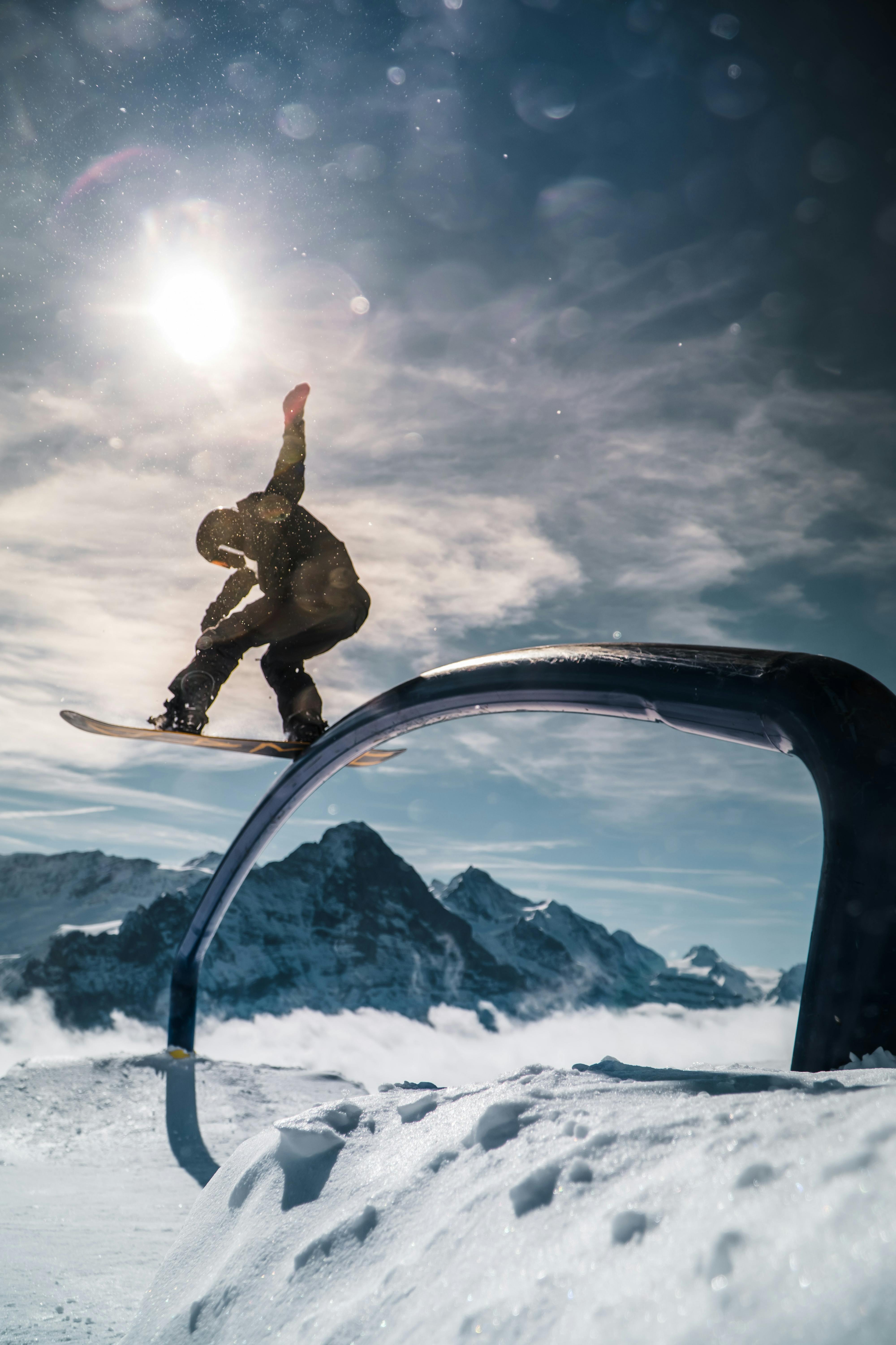 Snowboarder slides across rail sideways on his board. There are mountains in the background and a blue sky.