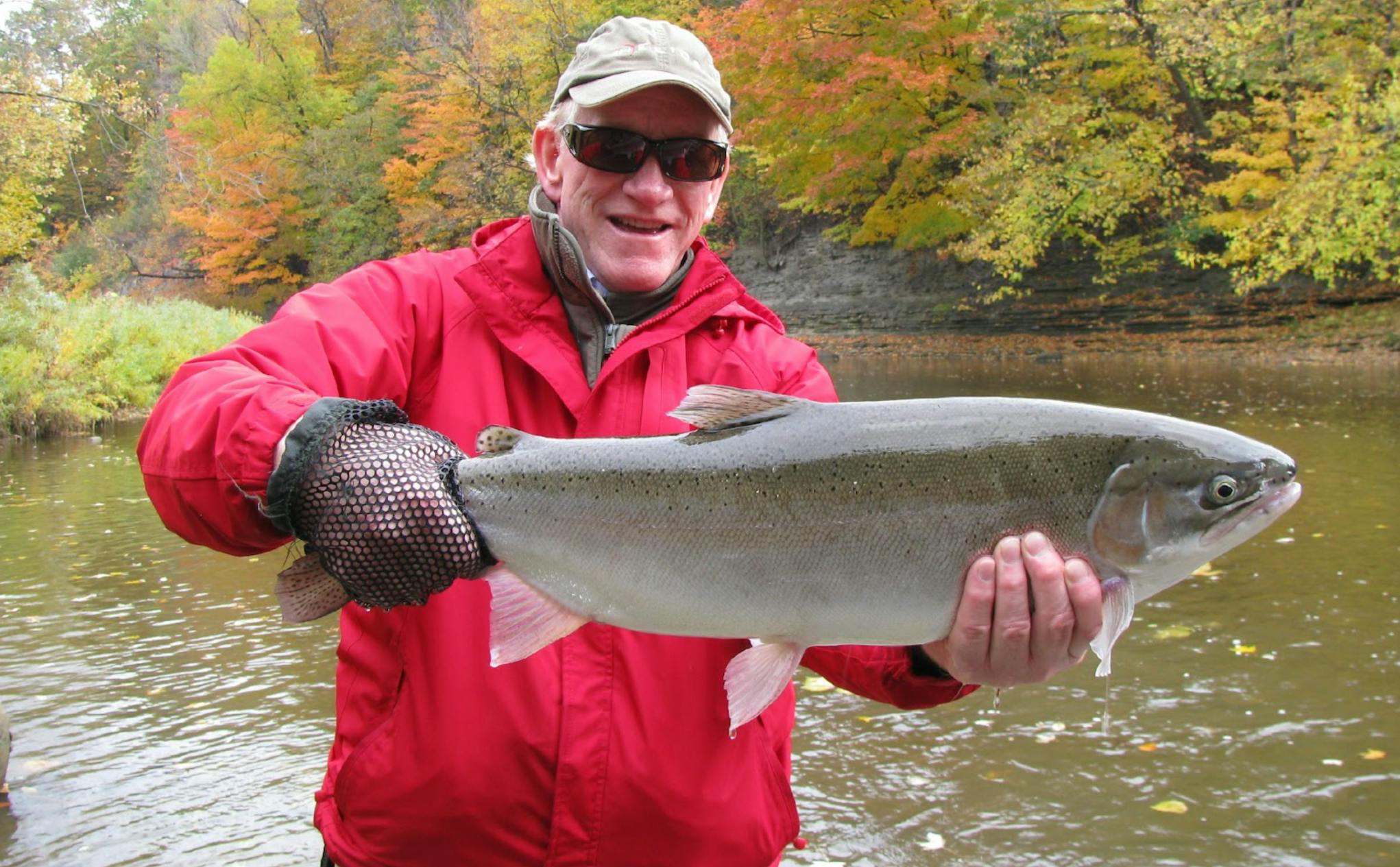 A man holding a Lake Erie Steelhead Fish while standing in a river.