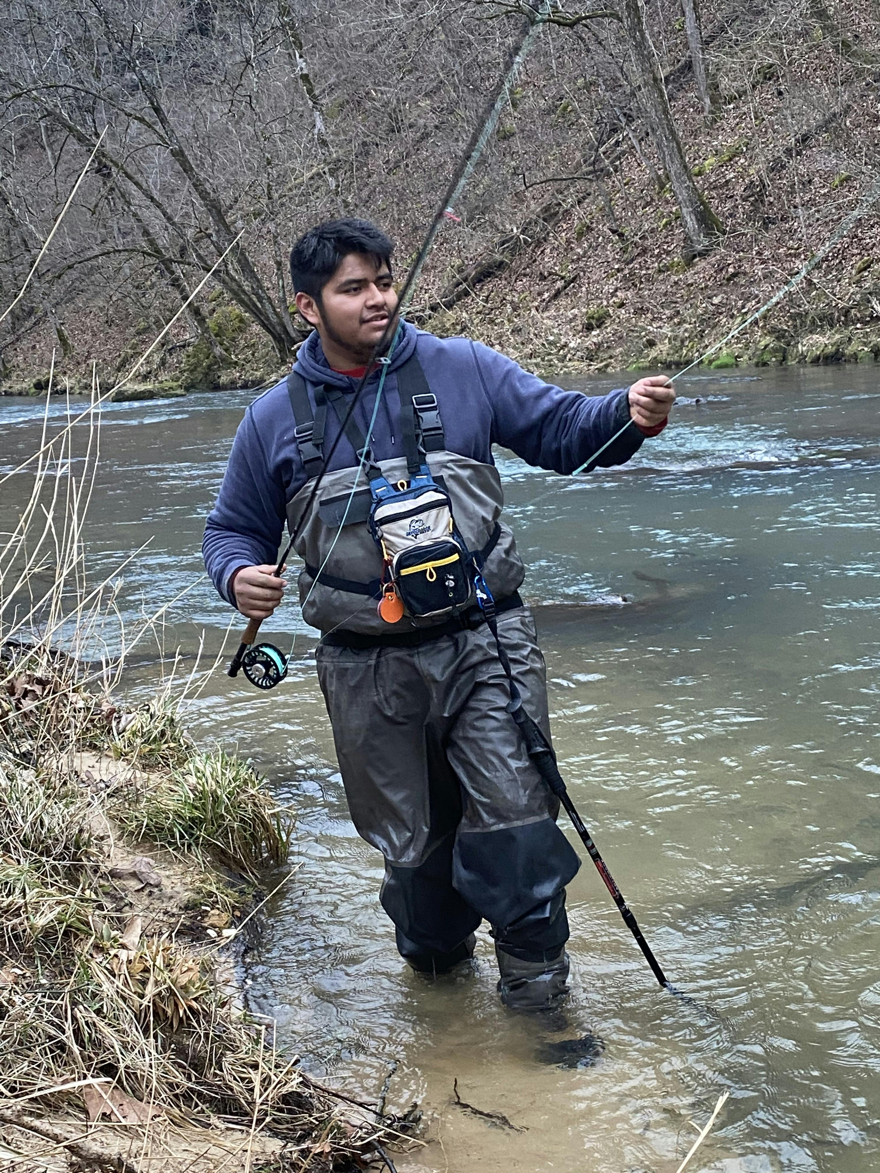 A young man holding a fly fishing reels and wearing waders.