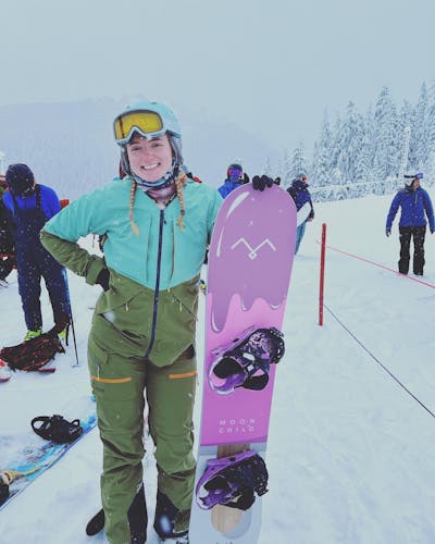A girl stands with her snowboard in line at a ski resort.