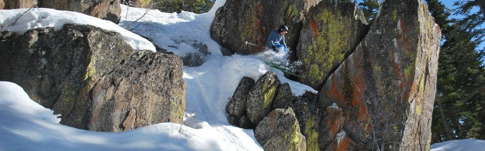 A skier executing a jump off snow-covered boulders