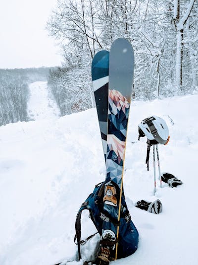 A pair of skis sticking up in the snow. There are trees covered in snow in the background.