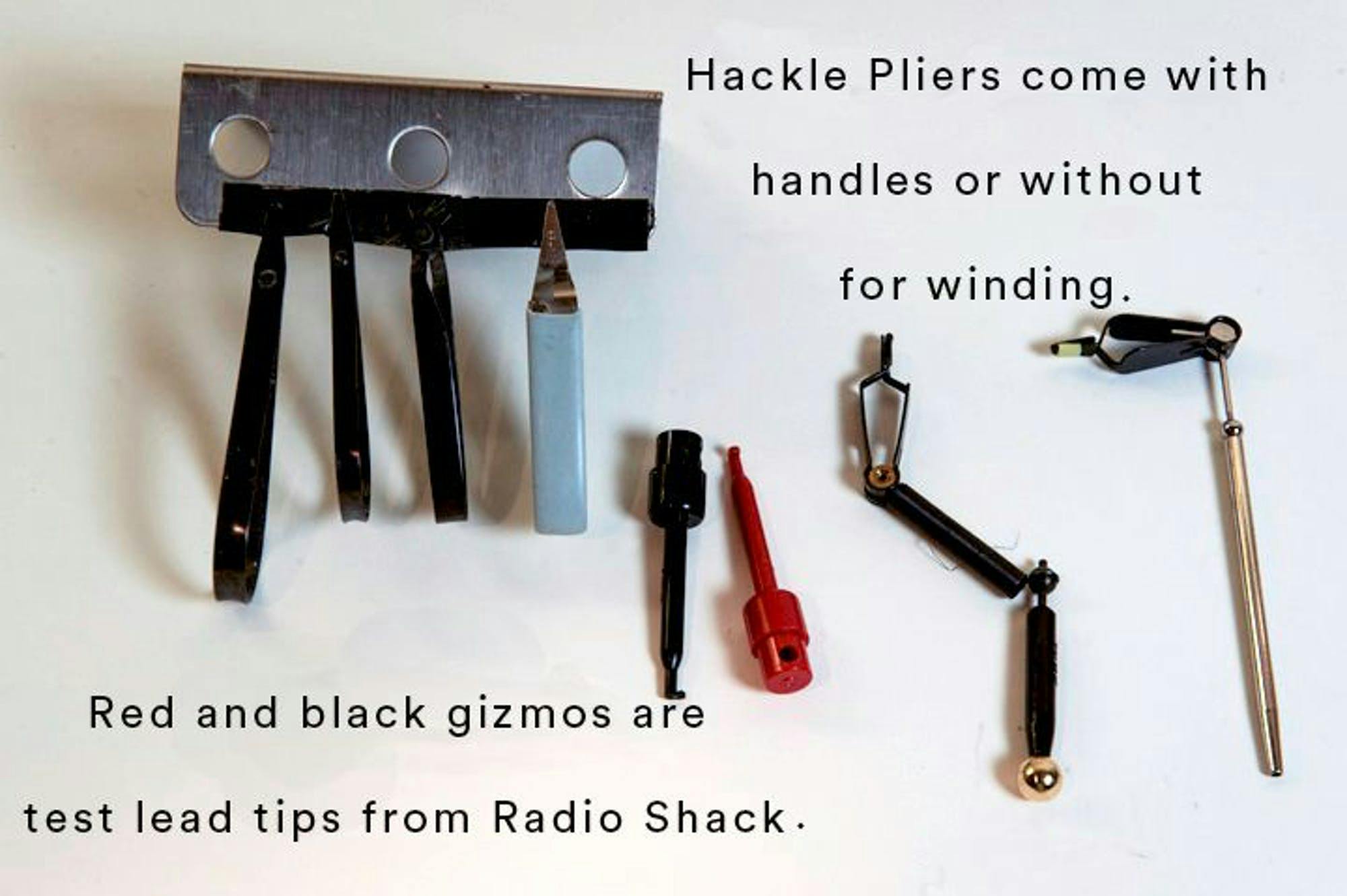 An image of hackle pliers and an assortment of tools on a white background. The text reads, "Hackle pliers come with handles or without for winding. Red and black gizmos are test lead tips from Radio Shack."