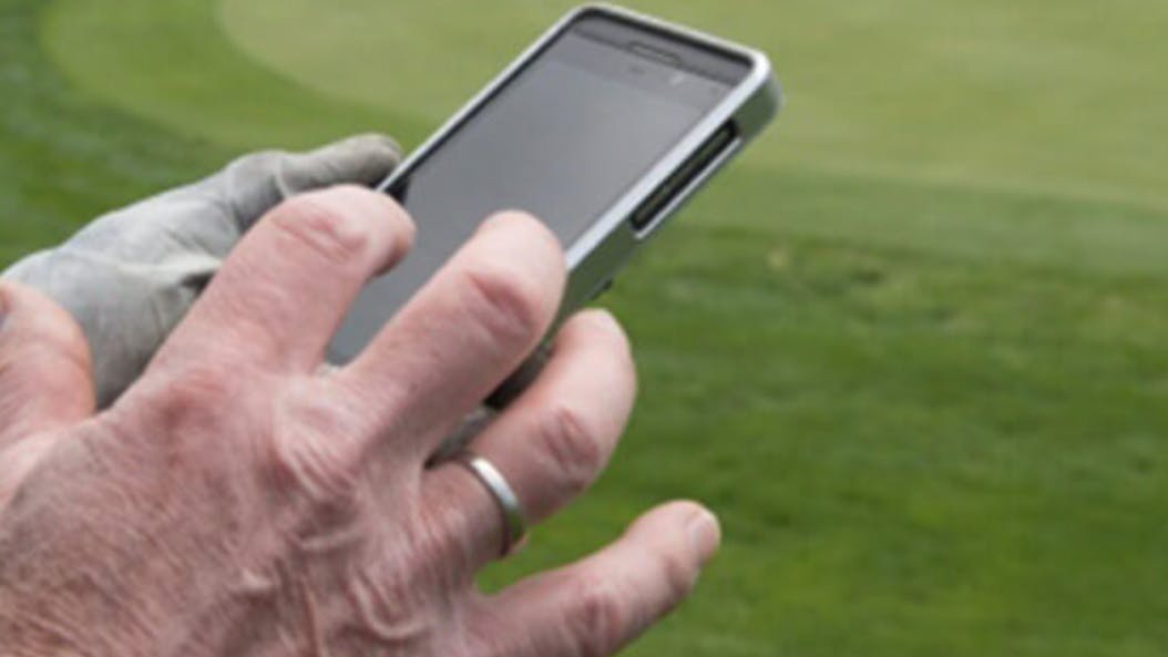 A man with one golf glove on types on a phone with the other hand. He is at a golf course.