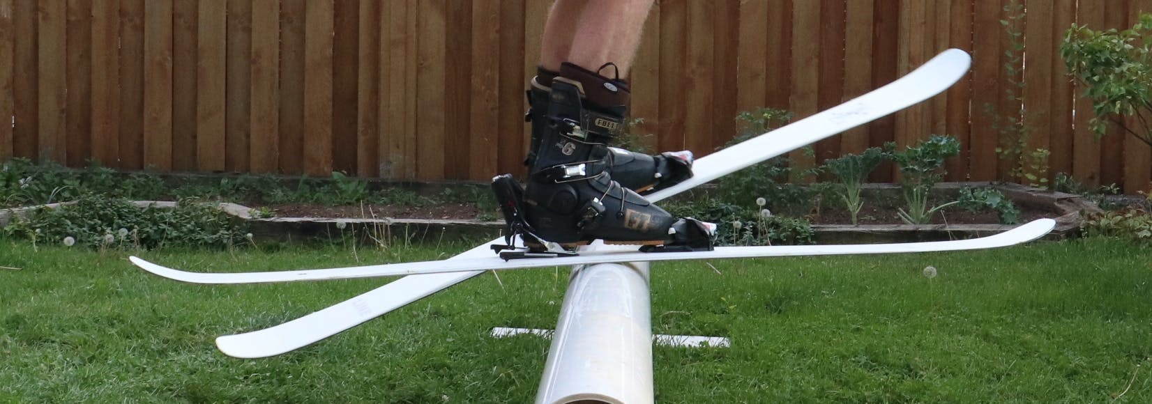 A skier using skis on a rail in the backyard with grass. 